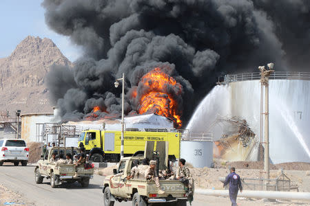 Soldiers ride on patrol trucks driving past an oil storage tank engulfed by fire at the Aden oil refinery one day after an explosion in the refinery in Aden, Yemen January 12, 2019. REUTERS/Fawaz Salman