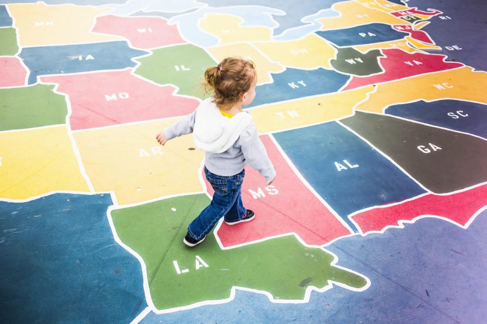 An image of a young girl walking on top of a map of the United States at a playground.