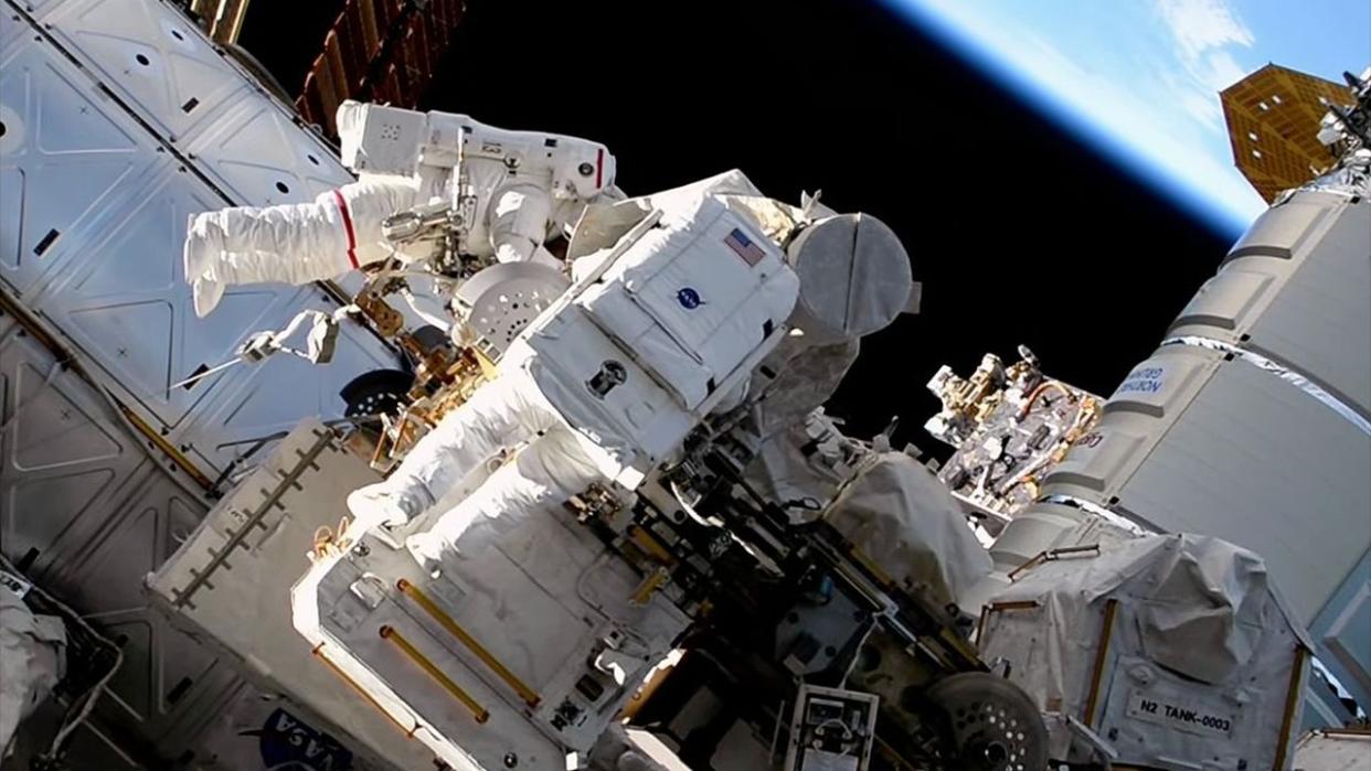  Two astronauts in spacesuits on the outside of a space station with Earth in the background. 