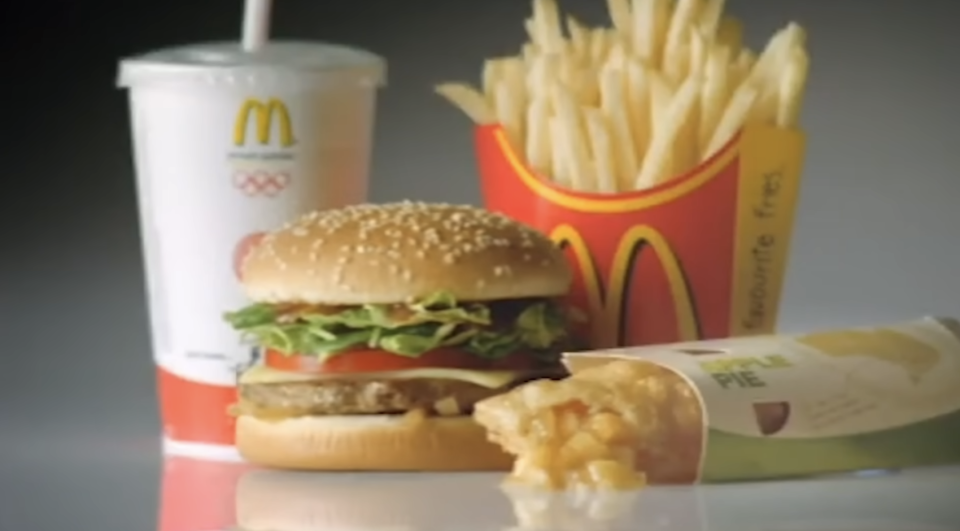 McDonald's meal featuring a sesame seed hamburger, fries in a red container, apple pie, and a soft drink cup