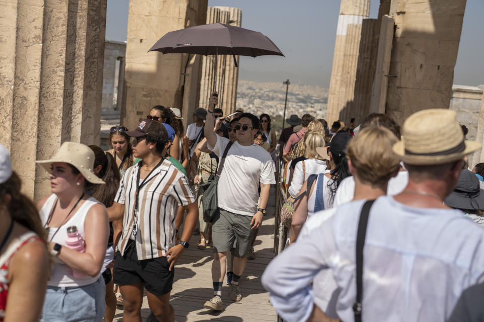 A man holds an umbrella as he and other tourists enters the ancient Acropolis hill during a heat wave, in Athens, Greece, Thursday, July 13, 2023. The government has announced emergency measures this week, allowing workers to stay home during peak temperature hours as a heat wave is due to affects most of Greece. (AP Photo/Petros Giannakouris)