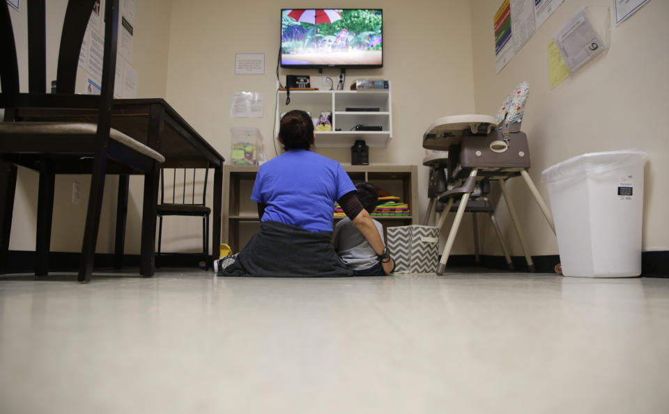 A Comprehensive Health Services caregiver watches TV with a young migrant at a "tender-age" facility for babies, children and teens, in Texas' Rio Grande Valley, Thursday, Aug. 29, 2019, in San Benito, Texas. Sheltering migrant children has become a booming business for Comprehensive Health Services, a Florida-based government contractor, as the number of children in government custody has swollen to record levels over the past two years. (AP Photo/Eric Gay)