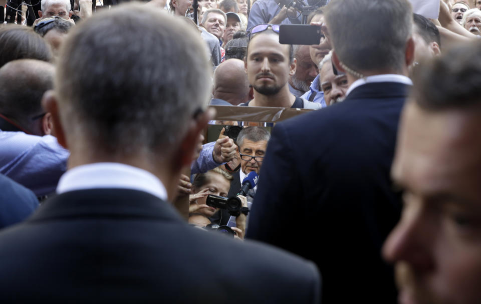 A protester holds a mirror in front of Czech Republic's Prime Minister Andrej Babis, front left, while delivering a speech to honor the victims of the Soviet-led invasion of Czechoslovakia in 1968 at a ceremony in Prague, Czech Republic, Tuesday, Aug. 21, 2018. Dozens of protesters gathered to oppose the prime minister. Babis, a populist billionaire, is a controversial figure for many due to a power-sharing deal with the maverick Communist Party and fraud charges he is facing. His position is also complicated by allegations he collaborated with the former communist-era secret police. (AP Photo/Petr David Josek)