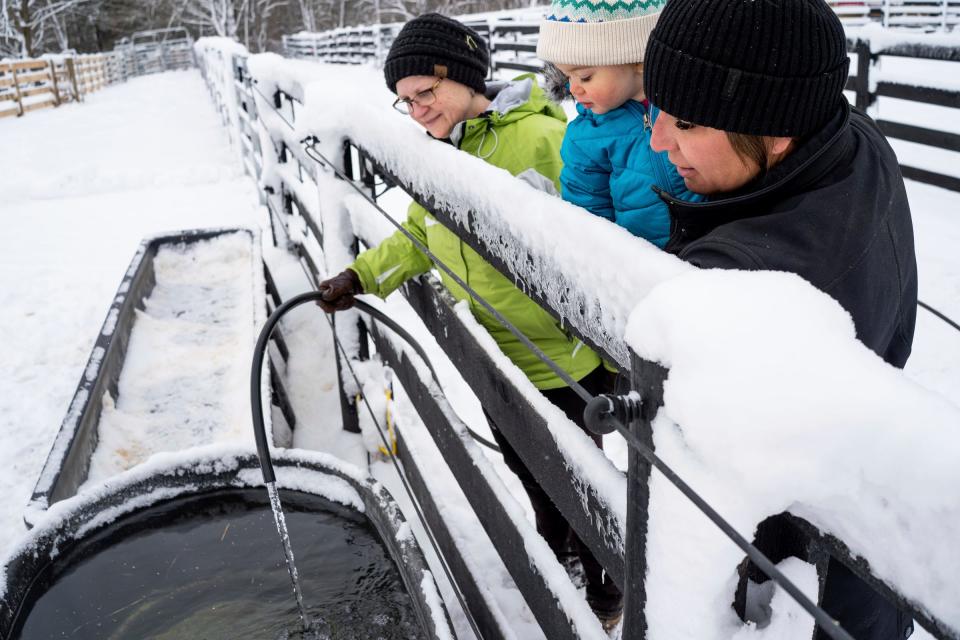 Abraham Ranch volunteer Kay Hehl, right, holds the owner's daughter, Ivy Abraham, while watching as volunteer Beth Anne Hillebrand fills water for animals at Abraham Ranch in Clarkston on Thursday, January 18, 2024, after clearing a frozen hose.