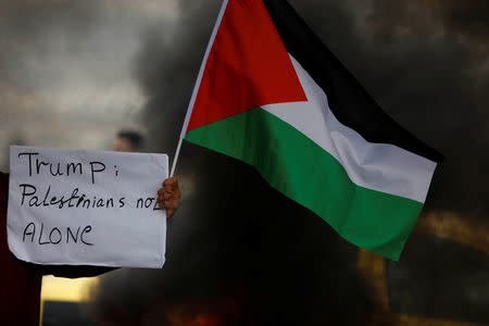 A demonstrator holds a sign and a Palestinian flag during clashes with Israeli troops at a protest against U.S. President Donald Trump's decision to recognise Jerusalem as the capital of Israel, near the West Bank city of Nablus, December 29, 2017. REUTERS/Mohamad Torokman