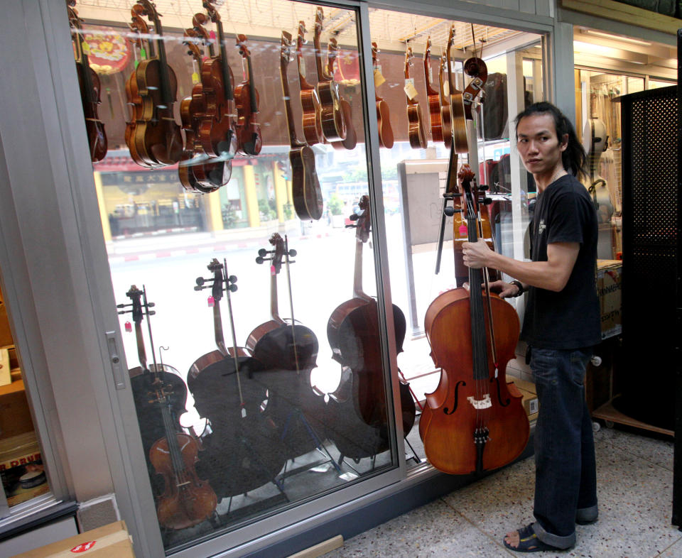 A shop assistant picks up a cello out of the show window for customers at a musical instrument shop in Bangkok, Thailand, Friday, March 8, 2013. Delegates attending a global biodiversity conference in Bangkok this week are debating a U.S. proposal to streamline international customs checks for travelers with musical instruments that legally contain endangered wildlife products like exotic hardwoods, ivory or tortoise shell. (AP Photo/Sakchai Lalit)