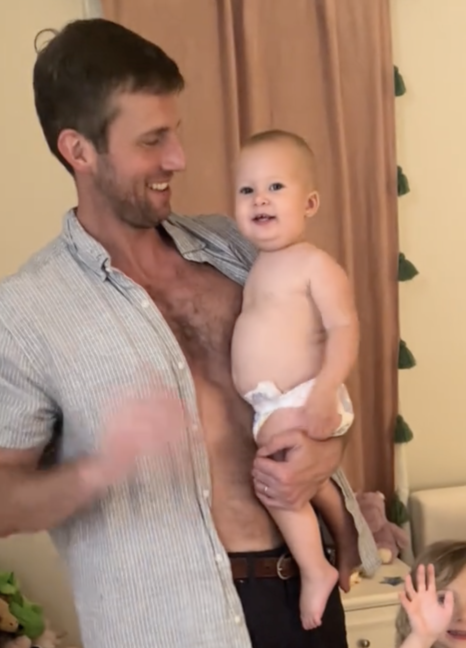 A smiling man holds a baby in a diaper