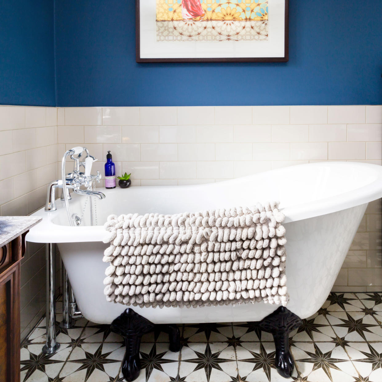  Roll top bath in a bathroom with dark blue walls and white tiles and a black and white patterned tiled floor. 