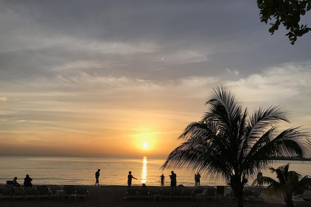 People are silhouetted on the beach during sunset in Negril, Jamacia