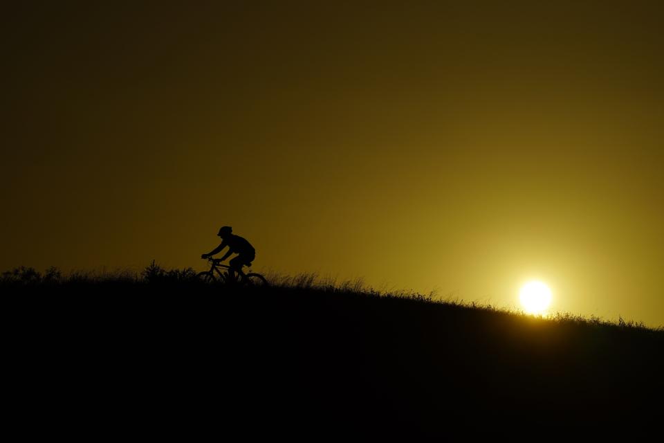 A cyclist moves up a hill during sunset, Monday, July 17, 2023, in San Antonio. (AP Photo/Eric Gay)