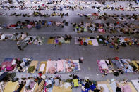 Migrant workers and their families rest in an exhibition hall after being evacuated from their workplaces in Hangzhou in eastern China's Zhejiang province Sunday, July 25, 2021. A typhoon blew heavy rain across the Shanghai region Monday, leaving roads and low-lying areas waterlogged and felling billboards and signs on its second landfall in eastern China. (Chinatopix via AP)