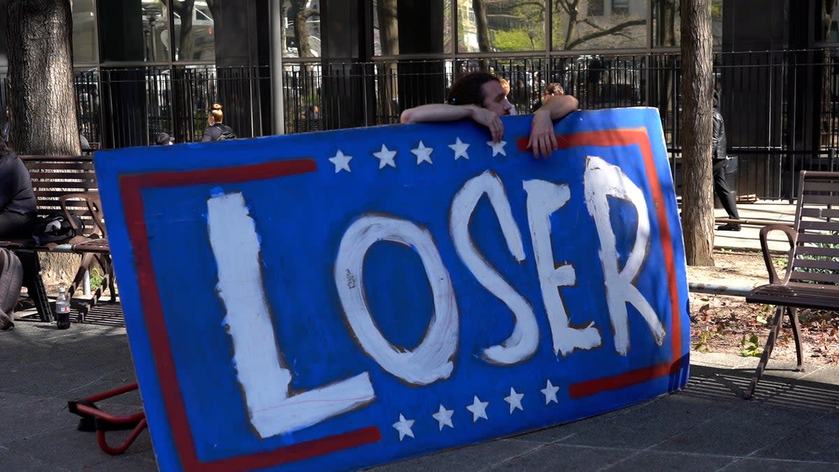 A man holds a protest sign outside of court as former president Donald Trump’s trial begins (Natalie Chinn / The The Independent)