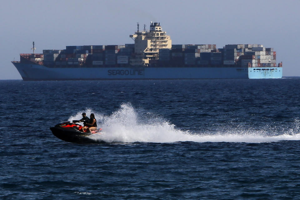 Un hombre y una mujer conducen una moto de agua frente a un buque de carga en la ciudad costera del sur de Limassol, Chipre, el miércoles 29 de julio de 2020. (AP Photo / Petros Karadjias)