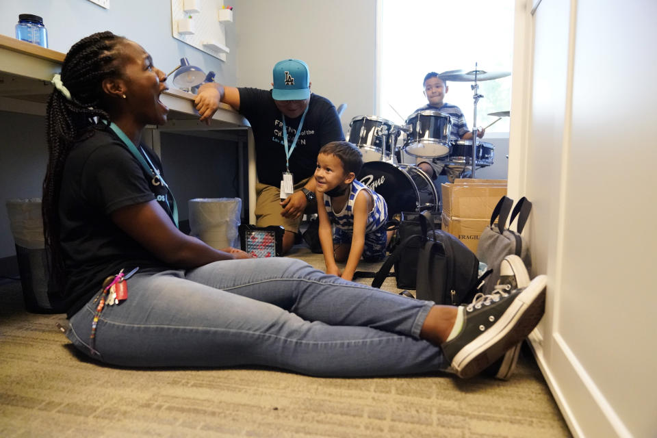 Mentors Ashakia Morgan, left, and Angel Garcia, top center, chat with Aleksander Robinson, 7, while playing battleship as Issac Portillo,8, top right, plays the drums at a Friends of the Children office Wednesday, Aug. 24, 2022, in Lancaster, Calif. Billionaire philanthropist MacKenzie Scott donated $44 million to the Oregon-based mentoring organization, Friends of the Children, which supports children at risk of entering the welfare system by pairing them with a longtime mentor. (AP Photo/Marcio Jose Sanchez)