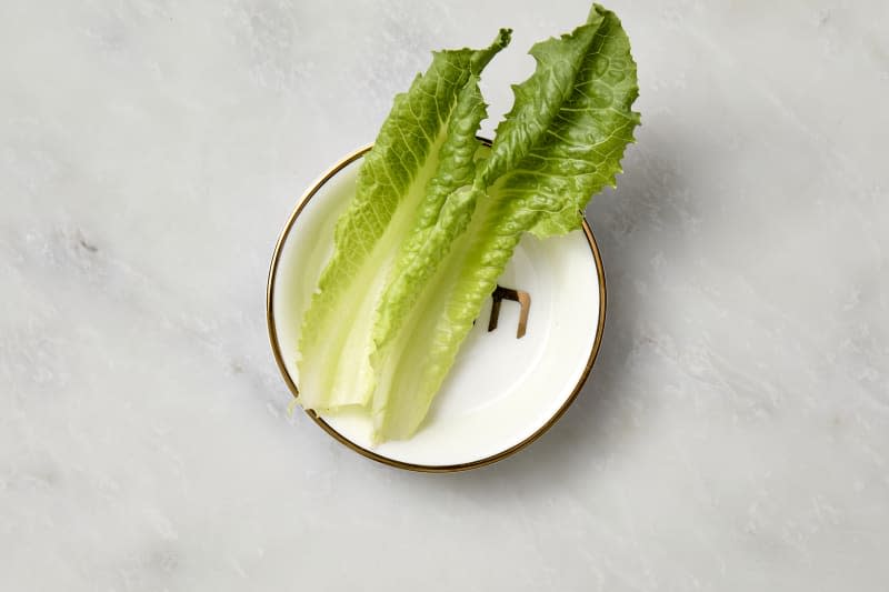 overhead shot of two lettuce leaves on a small white plate with a gold rim.