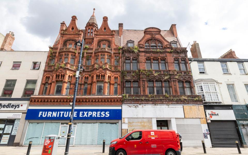 The red terracotta building above a boarded-up Furniture Express and covered in weeds