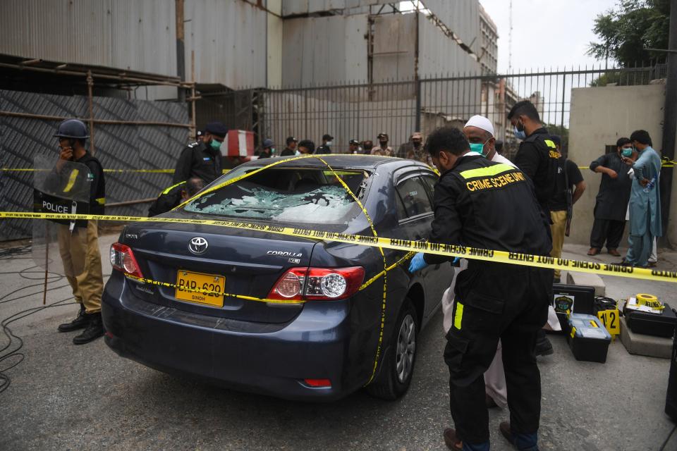 TOPSHOT - Policemen guard as members of Crime Scene Unit investigate around a car used by alleged gunmen at the main entrance of the Pakistan Stock Exchange building in Karachi on June 29, 2020. - Gunmen attacked the Pakistan Stock Exchange in Karachi on June 29, with four of the assailants killed, police said. (Photo by Asif HASSAN / AFP) (Photo by ASIF HASSAN/AFP via Getty Images)