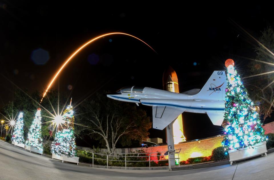 A SpaceX Falcon 9 rocket flies beyond decorated Christmas trees, a NASA T-38 display and a space shuttle external tank display early Thursday morning at the Kennedy Space Center Visitor Complex.