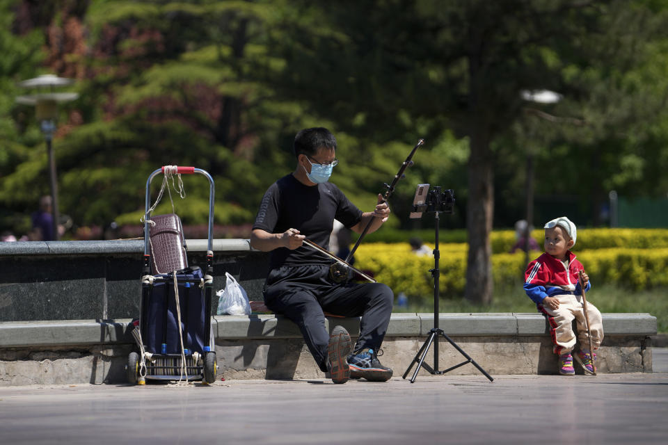 A child looks at a resident wearing a face mask plays a traditional music instrument outside the closed Chaoyang Park due to pandemic measures by authorities on Sunday, May 15, 2022, in Beijing. (AP Photo/Andy Wong)