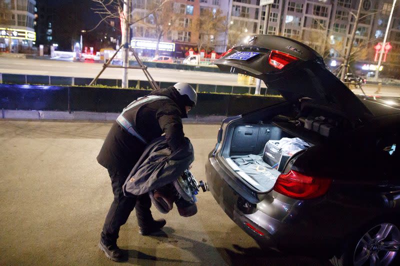 Liu Pengfei, a substitute driver of ride-hailing service platform DiDi Chuxing, unloads his electric bike from the boot of a client's car in Beijing