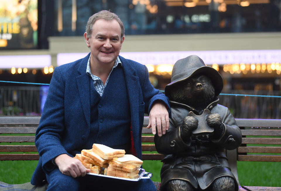 Hugh Bonneville eating a marmalade sandwich alongside a Paddington Bear statue as he attends the Scenes In The Square statue trail unveiling in Leicester Square, London. (Photo by Victoria Jones/PA Images via Getty Images)