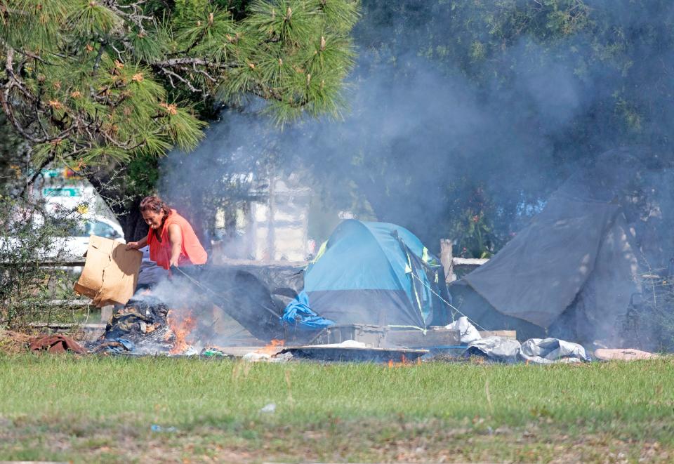 A woman collects and burns trash and garbage at a homeless campsite at Brentwood Park off North Palafox on Friday, March 10, 2023. 