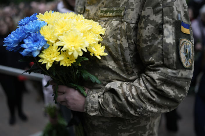 A military member holds flowers in the Ukrainian colors of yellow and blue.