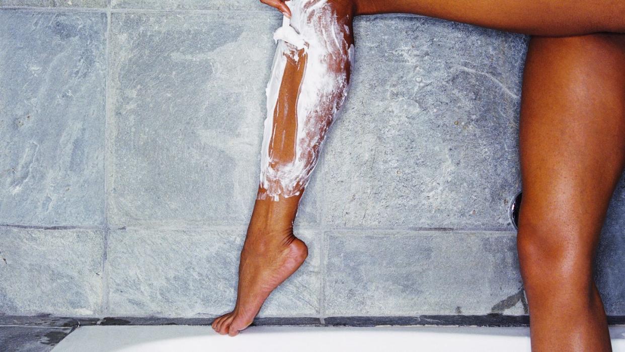 woman shaving legs with shaving cream and razor