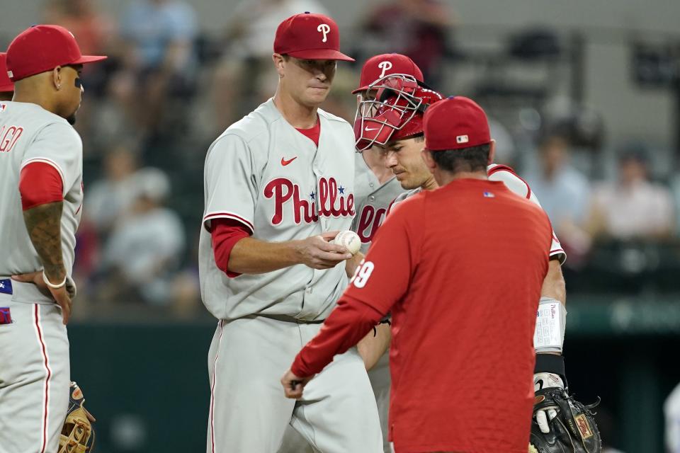 Philadelphia Phillies' Johan Camargo, left, and catcher J.T. Realmuto stand on the mound as starting pitcher Kyle Gibson turns the ball over to interim manager Rob Thomson, front, in the seventh inning of a baseball game against the Texas Rangers, Tuesday, June 21, 2022, in Arlington, Texas. (AP Photo/Tony Gutierrez)