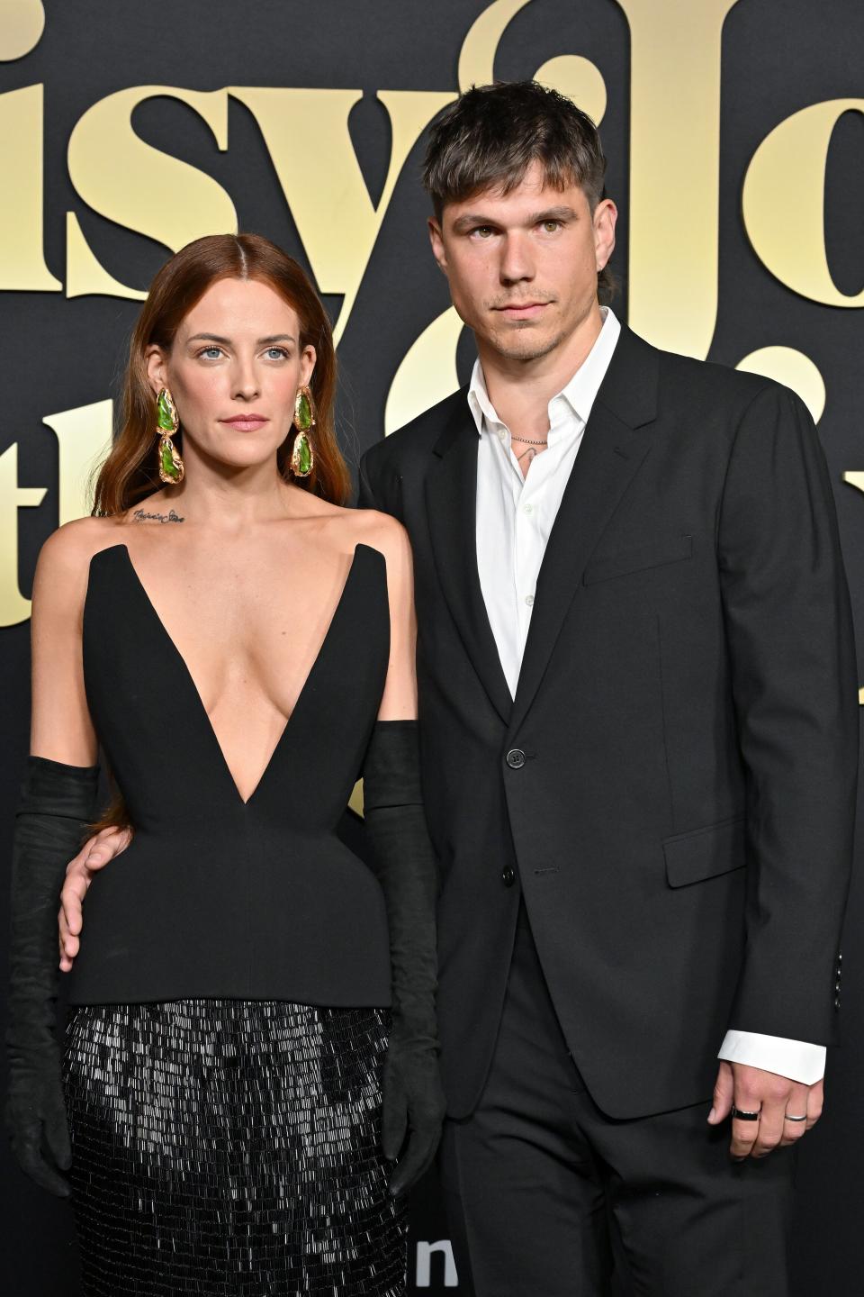 Riley Keough and Ben Smith-Petersen at a 'Daisy Jones & The Six' event. Riley wears a plunging black dress with long gloves, and Ben is in a black suit