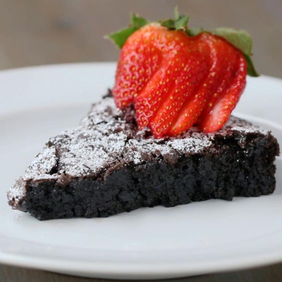 A dense slice of chocolate cake with icing sugar and sliced strawberries