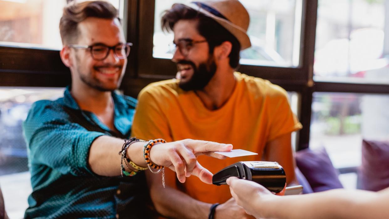 Two gay men pay in bar  with credit card.