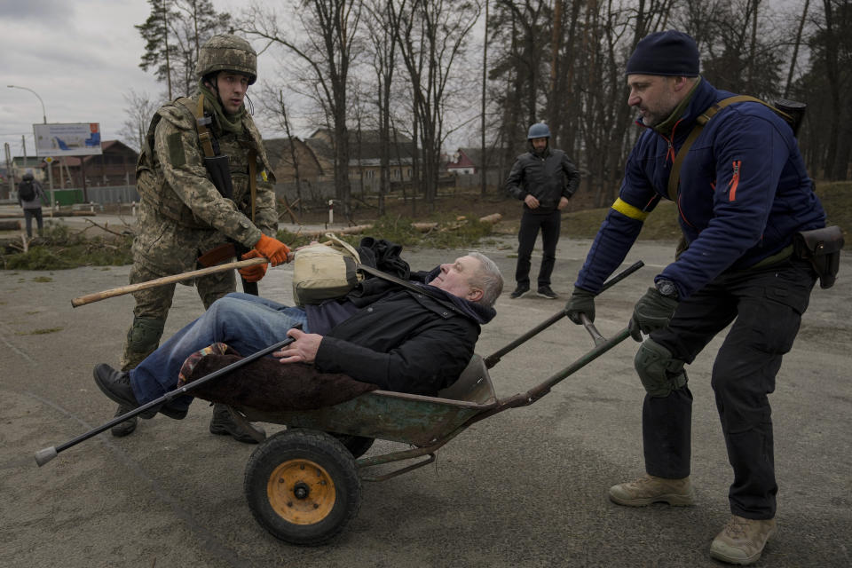 A man is helped in a wheelbarrow after crossing on an improvised path under a bridge that was destroyed by a Russian airstrike, as people flee the town of Irpin, Ukraine, Saturday, March 5, 2022. What looked like a breakthrough cease-fire to evacuate residents from two cities in Ukraine quickly fell apart Saturday as Ukrainian officials said shelling had halted the work to remove civilians hours after Russia announced the deal. (AP Photo/Vadim Ghirda)