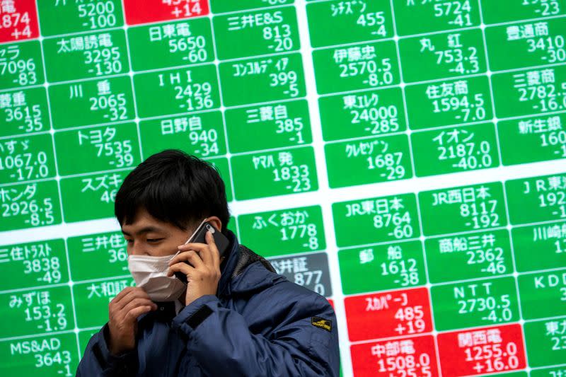 FILE PHOTO: A man wearing a protective face mask talks on his mobile phone in front of a screen showing the Nikkei index in Tokyo