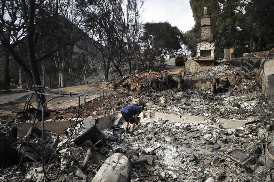 FILE - In this Nov. 13, 2018, file photo, Roger Kelton searches through the remains of his mother-in-law's home leveled by the Woolsey fire, in the southern California city of Agoura Hills. Southern California Edison has reached an agreement with state regulators on Thursday, Dec. 16 2021, for more than half a billion dollars in penalties related to five wildfires, including the Woolsey fire. (AP Photo/Jae C. Hong, File)