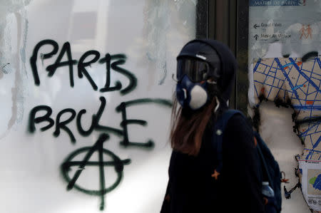 A protester walks past a graffiti during a demonstration by the "yellow vests" movement in Paris, France, March 16, 2019. The graffiti reads: "Paris burns." REUTERS/Benoit Tessier