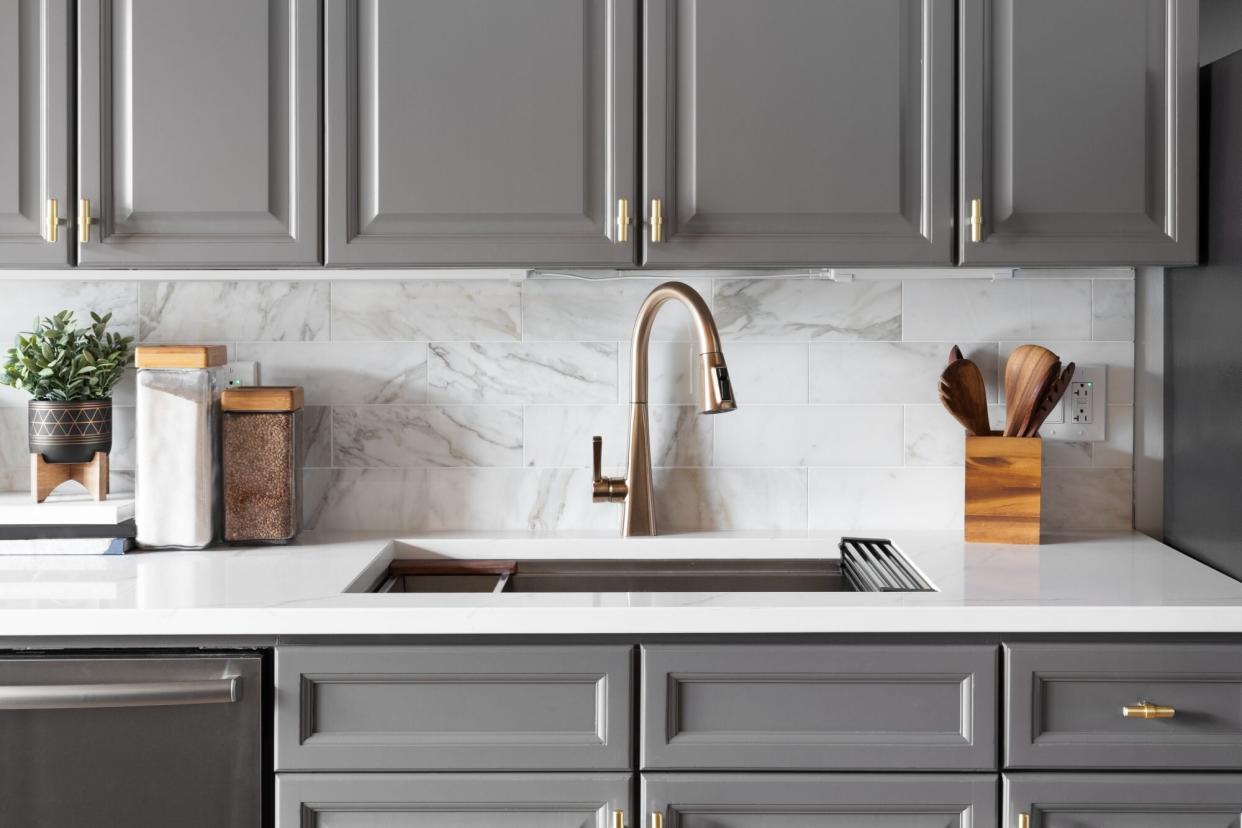 A gold kitchen faucet detail with grey cabinets