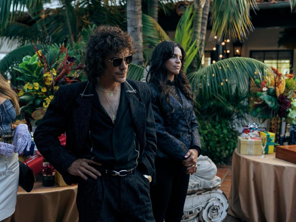rivi and carmen in griselda, standing amid palm trees and decorated tables with presents at a party