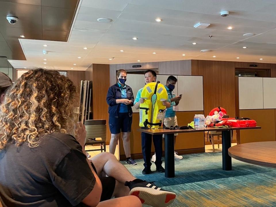 Cruise ship crew members show passengers how to properly put on a life vest during the muster drill.