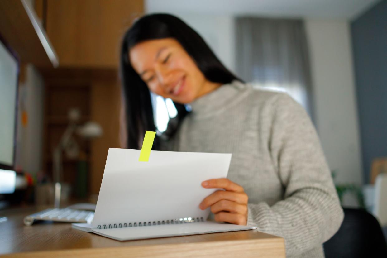 A young asian woman holds a notepad with colorful page markers, symbolizing organization and planning.