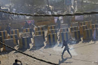 A farmer throws back a tear gas shells towards policemen, at the border between Delhi and Haryana state, Friday, Nov. 27, 2020. Thousands of agitating farmers in India faced tear gas and baton charge from police on Friday after they resumed their march to the capital against new farming laws that they fear will give more power to corporations and reduce their earnings. While trying to march towards New Delhi, the farmers, using their tractors, cleared concrete blockades, walls of shipping containers and horizontally parked trucks after police had set them up as barricades and dug trenches on highways to block roads leading to the capital. (AP Photo/Altaf Qadri)