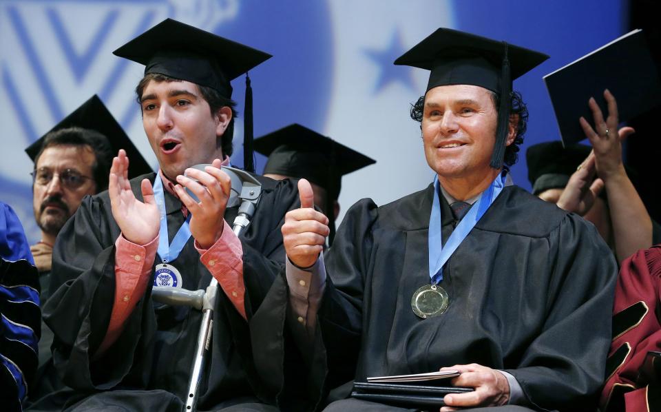 Boston Marathon bombing survivor Jeff Bauman, left, and spectator Carlos Arredondo react after both received honorary degrees during commencement ceremonies for Fisher College in Boston, Saturday, May 10, 2014. Bauman lost his legs in the attack. Bauman and Arrendondo, who saved Bauman's life the day of the bombing, each gave graduation speeches during the ceremony. (AP Photo/Michael Dwyer)