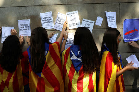 Young women wearing Esteladas (Catalan separatist flag) paste posters on the wall in support of the banned October 1st independence referendum in Barcelona, Spain, September 24, 2017. The posters read: "We vote to be free". REUTERS/Susana Vera