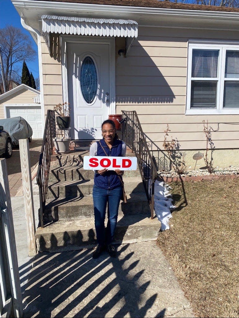 Kelsey Glavee, 29, holds a "sold" sign front of her new home purchased with help from OWN It's downpayment assistance program.