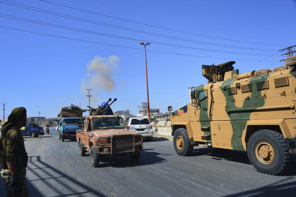 Smoke rises in the background from bombardment around the area as fighters with the Free Syrian army drive their pick-up truck, left, past a Turkey Armed Forces convoy, at a highway between Maaret al-Numan and Khan Sheikhoun in Idlib province, Syria, Monday, Aug. 19, 2019. The Turkish Defense Ministry says airstrikes have targeted a Turkish military convoy in Syria, killing at least three civilians and wounding 12 others in Monday's attack that occurred while the convoy was heading toward a Turkish observation post in the rebel-held stronghold of Idlib. (Murat Kibritoglu/DHA via AP)