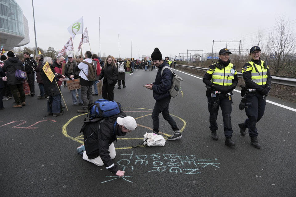 Police officers walk by climate activists blocking the main highway around Amsterdam near the former headquarters of a ING bank to protest its financing of fossil fuels, Saturday, Dec. 30, 2023. Protestors walked onto the road at midday, snarling traffic around the Dutch capital in the latest road blockade organized by the Dutch branch of Extinction Rebellion. (AP Photo/Patrick Post)