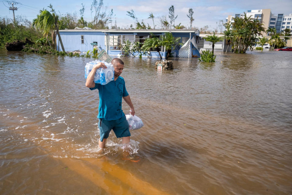 TOPSHOT - A man carrying bottled water wades through water in a flooded neighborhood in the aftermath of Hurricane Ian in Fort Myers, Florida, on September 29, 2022. - Hurricane Ian left a trail of devastation across Florida on Thursday with whole neighborhoods reduced to shattered ruins and millions left without power as US President Joe Biden warned of a high death toll. (Photo by Ricardo ARDUENGO / AFP) (Photo by RICARDO ARDUENGO/AFP via Getty Images)