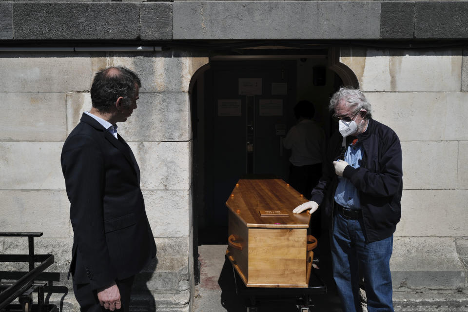 Paris undertaker Franck Vasseur, left, attends a funeral ceremony of a 75-year-old woman, with only the presence of her husband, right, at Pere Lachaise cemetery in Paris, Friday, April 24, 2020. Vasseur says that dealing with a flood of virus victims' bodies since March has turned his life into an infernal, head-spinning procession of death and that he feels robbed of his purpose by being unable to comfort families who cannot accompany bodies for cremation or gather in large numbers for funerals. (AP Photo/Francois Mori)