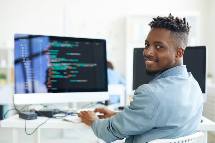 Computer programmer typing while looking at the camera