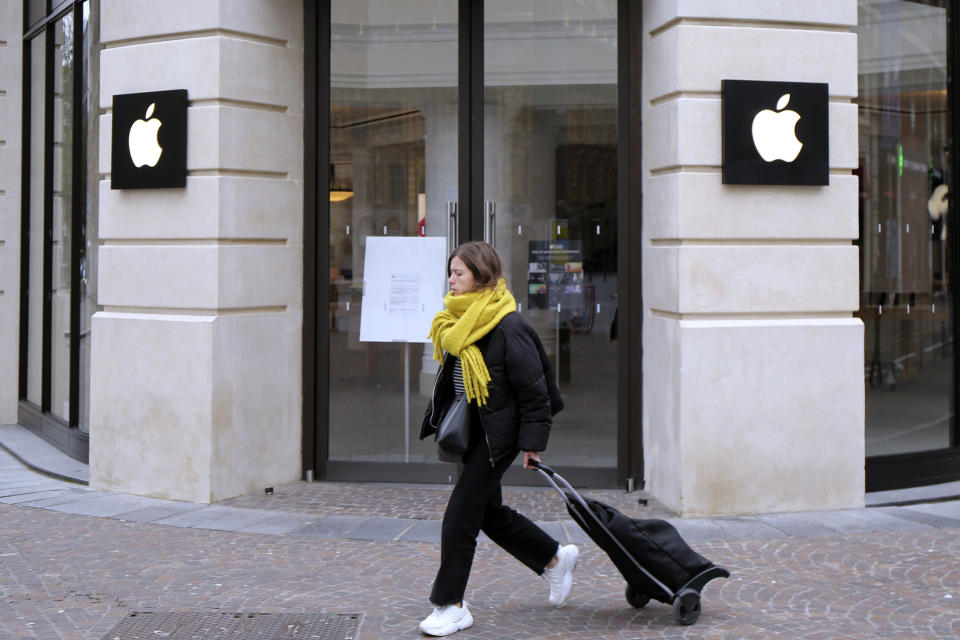 A woman in a yellow scarf walks past a closed Apple Store in Lille, northern France.